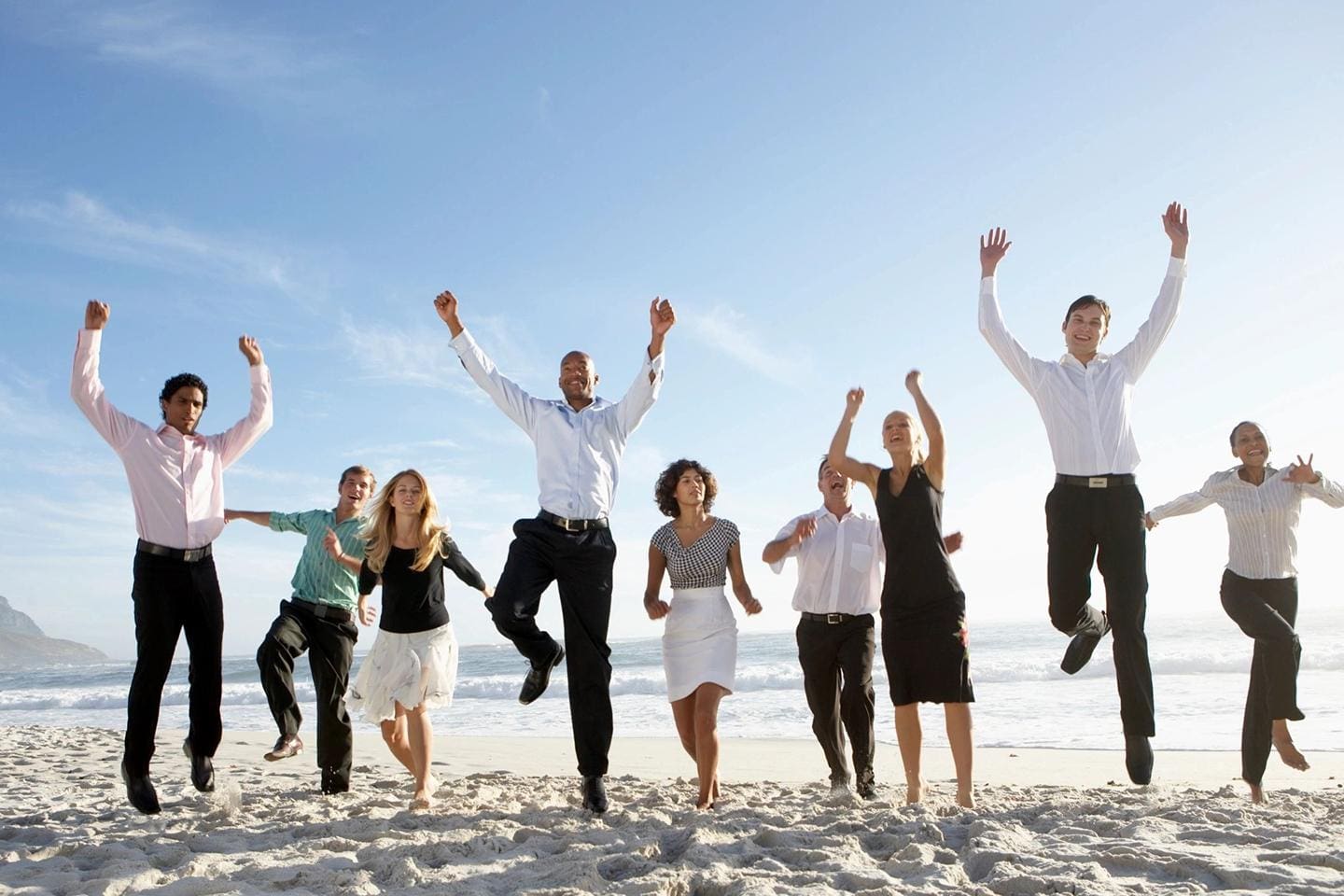 A group of people jumping up in the air on a beach.