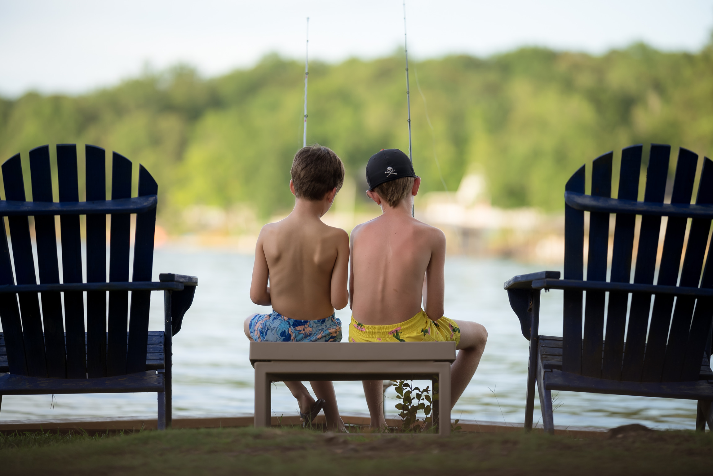 Two boys sitting on a bench near the water.